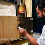 Man painting a piece of furniture a dark brown color.