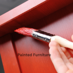 A piece of furniture and paint brush. Furniture being painted barn red. 