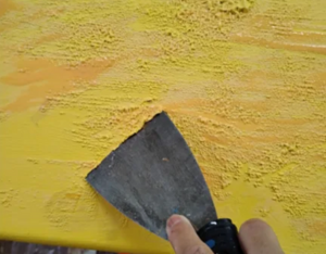 Scrapping the yellow paint with a putty knife