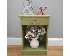 Green end table with vase and flowers, and sign and wood jack.