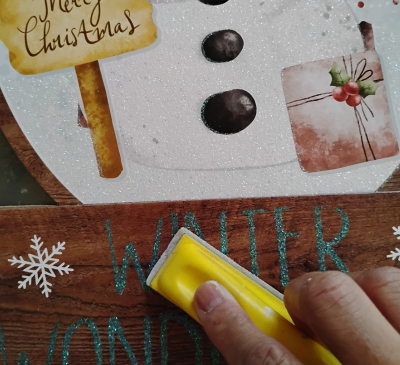 A hand sanding a Dollar Tree Christmas wall art.